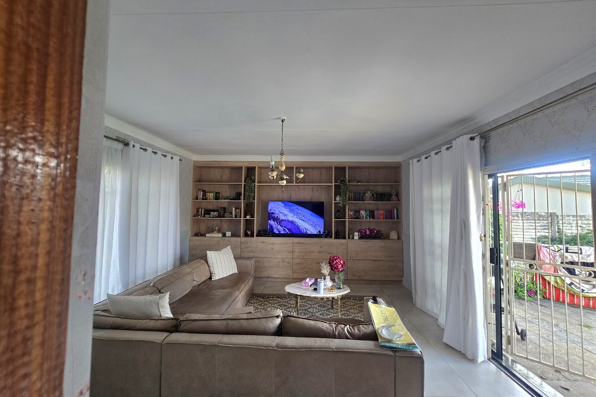 Spacious living room featuring a large built-in wooden shelving unit, tiled flooring, and direct access to the outdoor area through a sliding glass door.