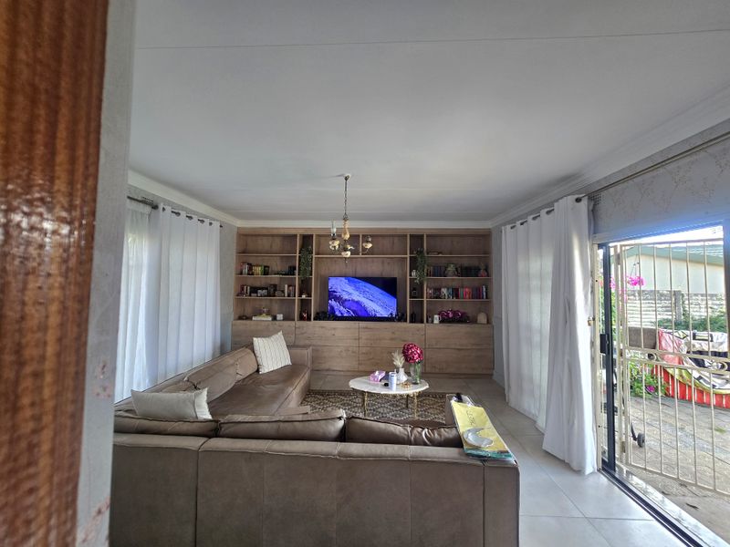 Spacious living room featuring a large built-in wooden shelving unit, tiled flooring, and direct access to the outdoor area through a sliding glass door.
