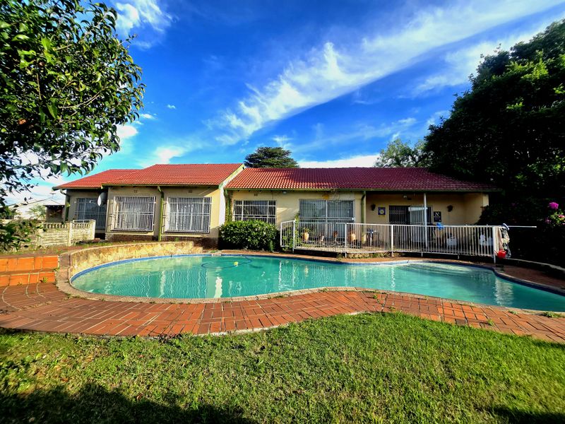 Rear view of the house featuring a swimming pool, brick paved surround, and a covered patio area with security bars on windows.