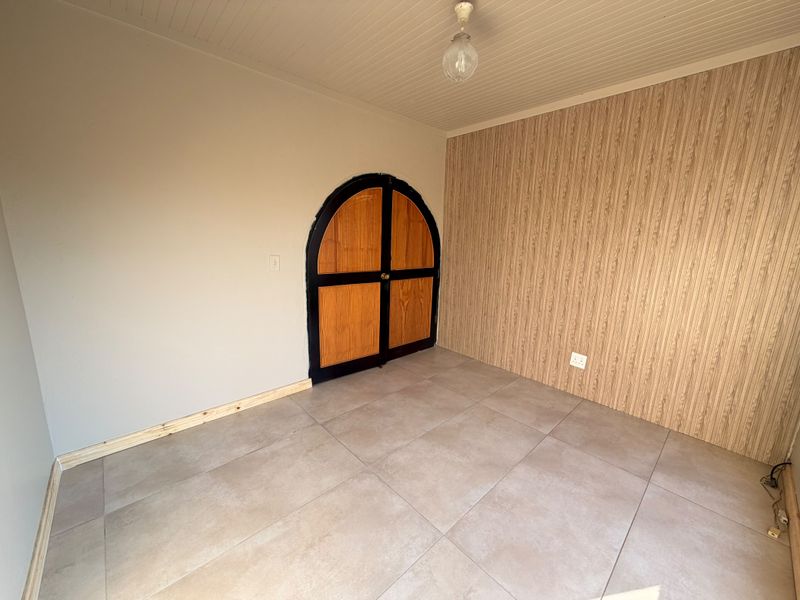 An empty bedroom featuring tiled flooring, wood-look wall paneling, a beadboard ceiling, and a distinctive arched double door entrance.