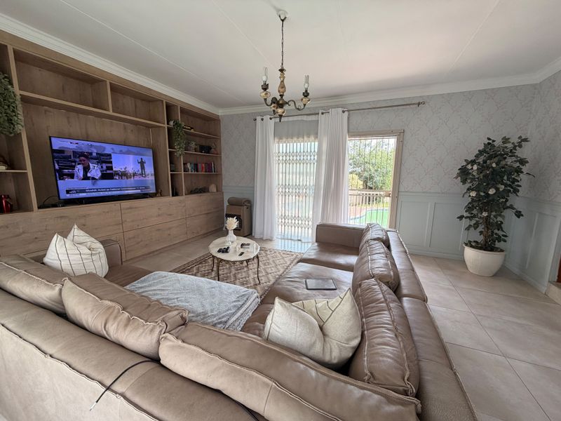 Spacious living room featuring a large built-in wooden shelving unit, tiled floors, decorative wainscoting, and direct access to the outdoor area through a sliding door.