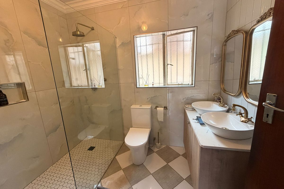 Modern bathroom featuring a spacious walk-in shower with glass screen, dual vessel sinks on a vanity cabinet, and elegant brass fixtures.