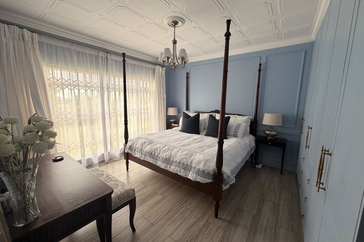 A well-maintained bedroom featuring elegant wall paneling, a decorative pressed metal ceiling, built-in cupboards, and wood-look tile flooring.