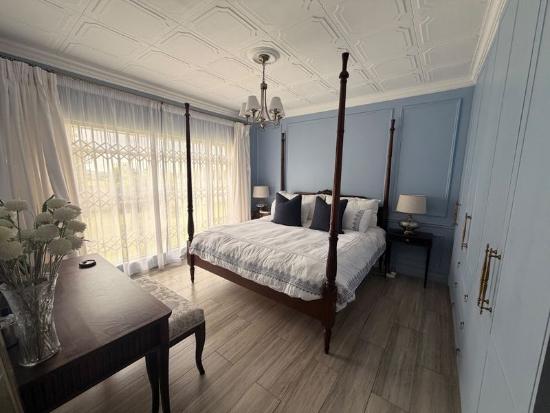 A well-maintained bedroom featuring elegant wall paneling, a decorative pressed metal ceiling, built-in cupboards, and wood-look tile flooring.