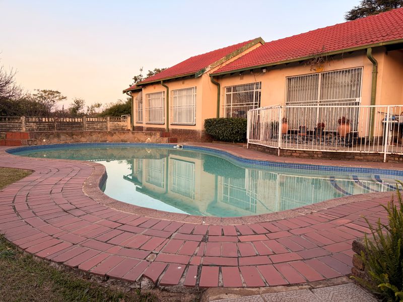 Rear exterior view featuring a swimming pool with a tiled surround, metal security fencing, and a single-story house with a tiled roof.