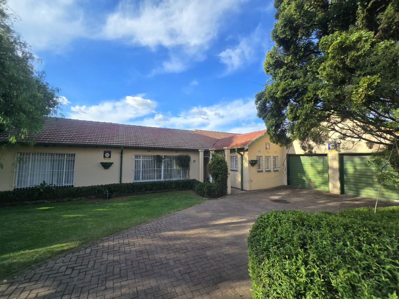 A well-maintained single-story house featuring a tiled roof, paved driveway, double garage, and established garden with security features.