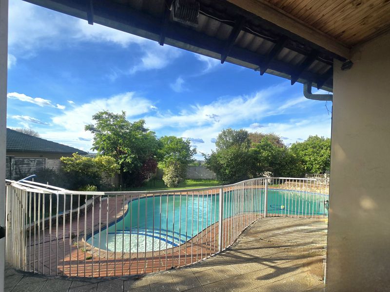 Outdoor pool area featuring a swimming pool with safety fencing, set within a private garden with a covered patio area.