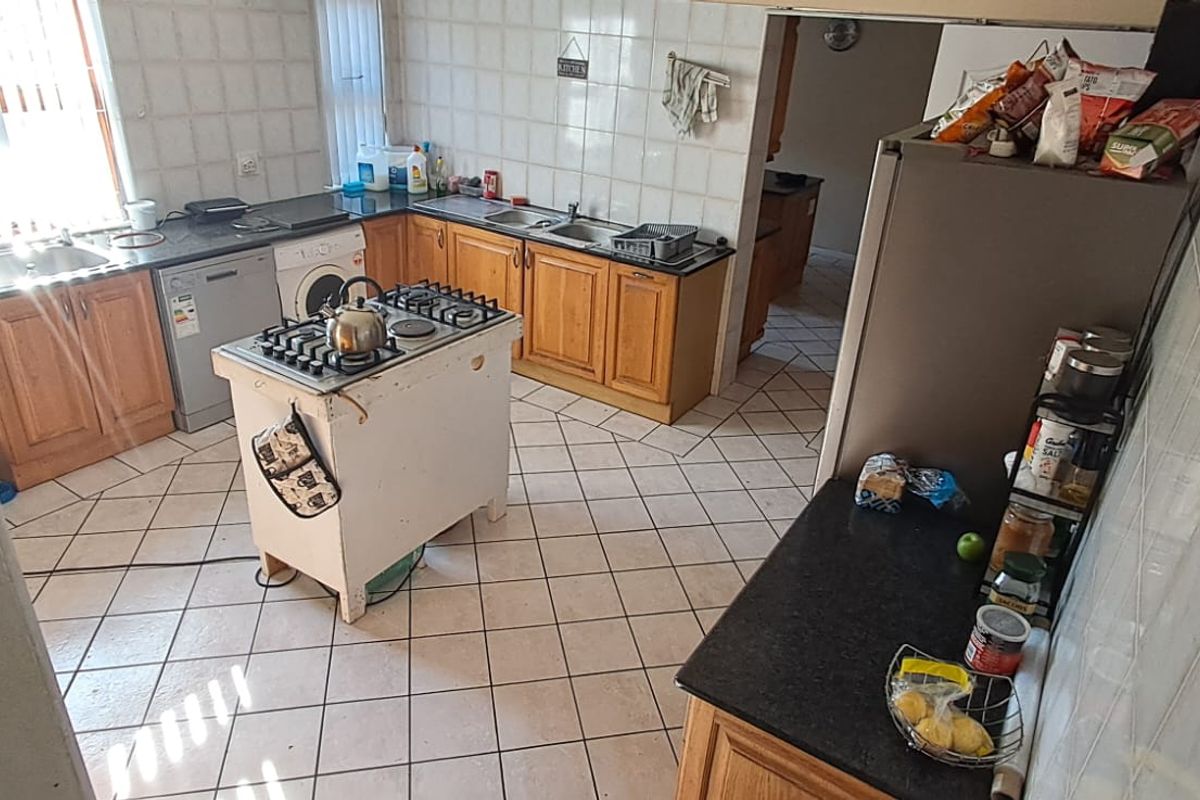 A functional kitchen featuring wooden cabinetry, tiled flooring, a central gas hob island, and a double sink with a tiled backsplash.