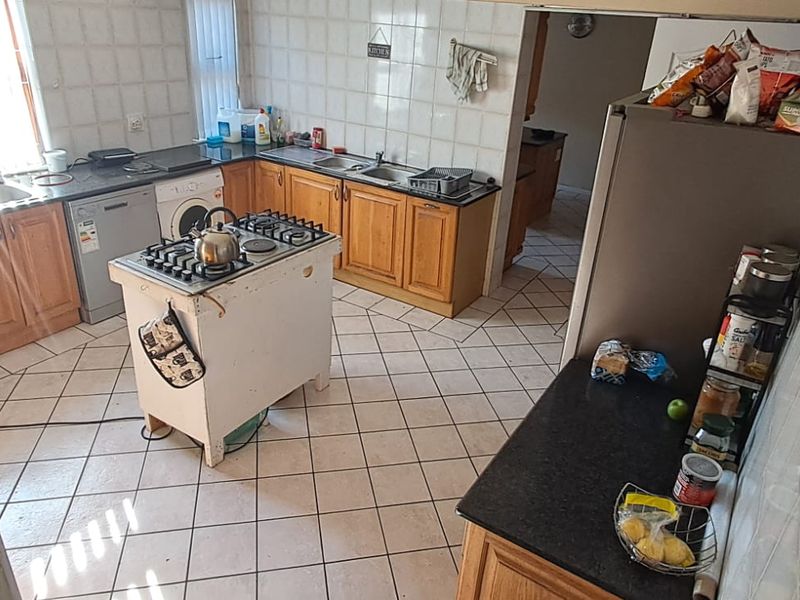 A functional kitchen featuring wooden cabinetry, tiled flooring, a central gas hob island, and a double sink with a tiled backsplash.