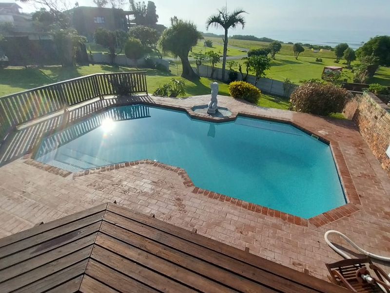 Outdoor pool area featuring a swimming pool with brick paving, timber decking, and a boundary wall, overlooking a spacious garden and coastal landscape.