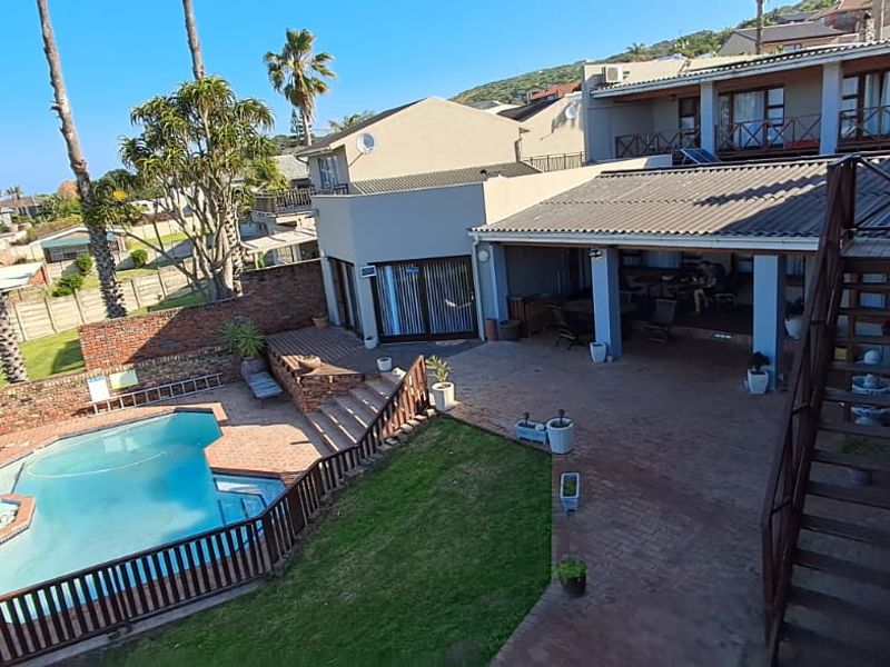 Rear exterior view featuring a swimming pool, paved patio area, lawn, and an external staircase leading to an upper balcony.