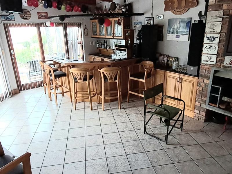 A dedicated bar area featuring a built-in counter, cabinetry, and a brick fireplace, with tiled flooring and direct access to the outdoor space.