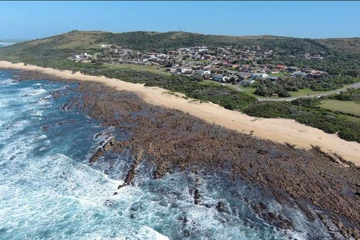 An aerial view of a coastal residential estate situated along a rocky shoreline and sandy beach.
