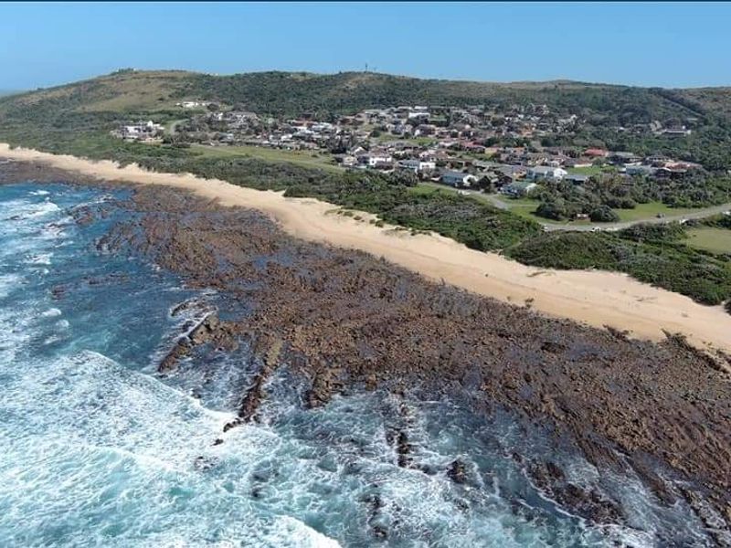An aerial view of a coastal residential estate situated along a rocky shoreline and sandy beach.