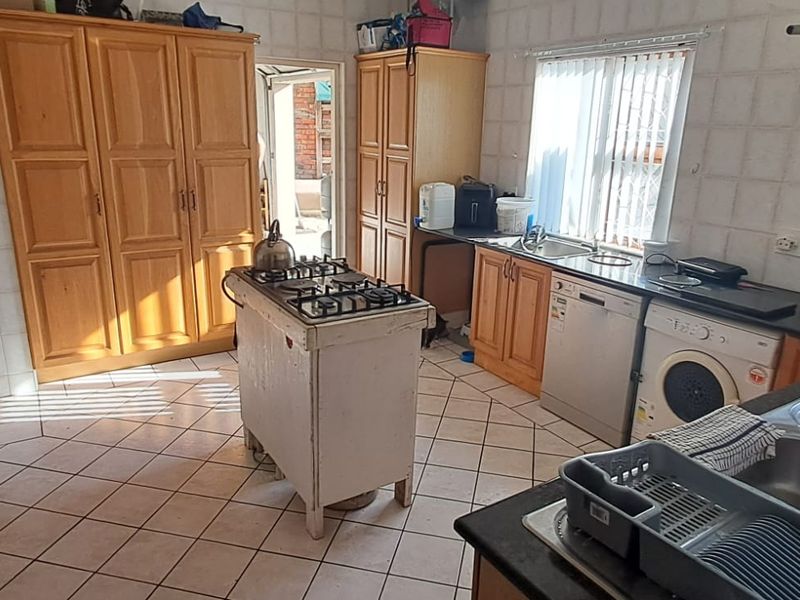 A functional kitchen featuring wooden cabinetry, tiled surfaces, a gas hob, and integrated appliances, offering potential for modernization and layout optimization.