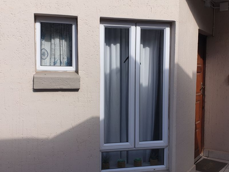 A view of the rear exterior facade featuring textured walls, white uPVC window frames, and a tiled patio area leading to a wooden entrance door.