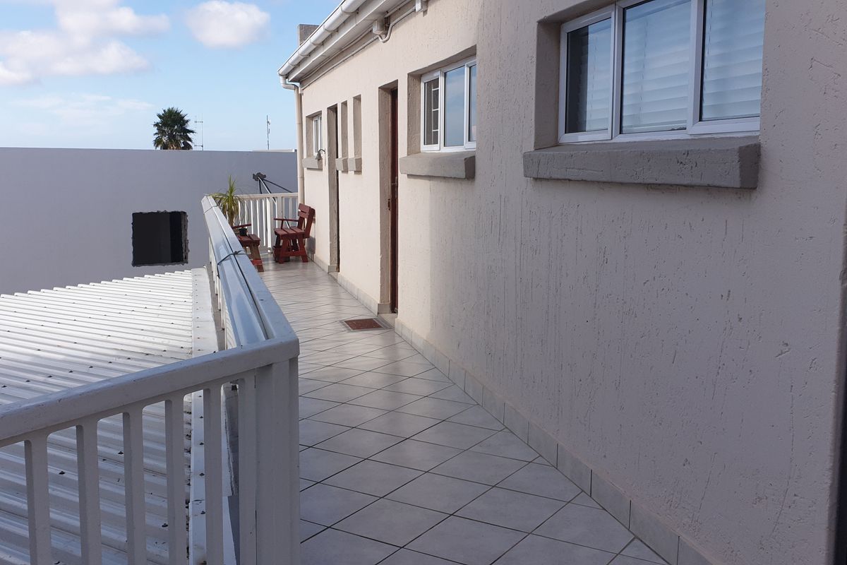 An exterior balcony featuring tiled flooring and a metal balustrade, providing access to the apartment unit.