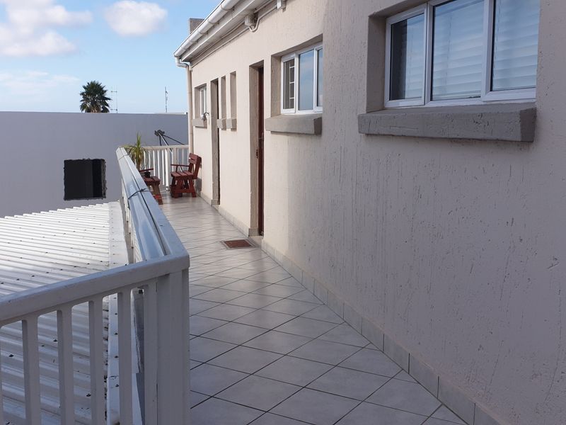 An exterior balcony featuring tiled flooring and a metal balustrade, providing access to the apartment unit.