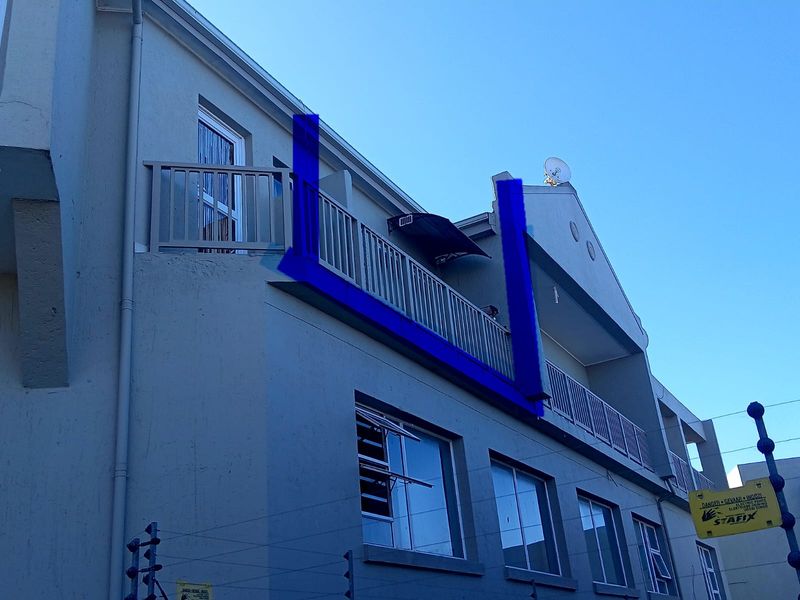 Exterior view of an apartment building featuring a balcony with a damaged balustrade section and installed electric fencing.