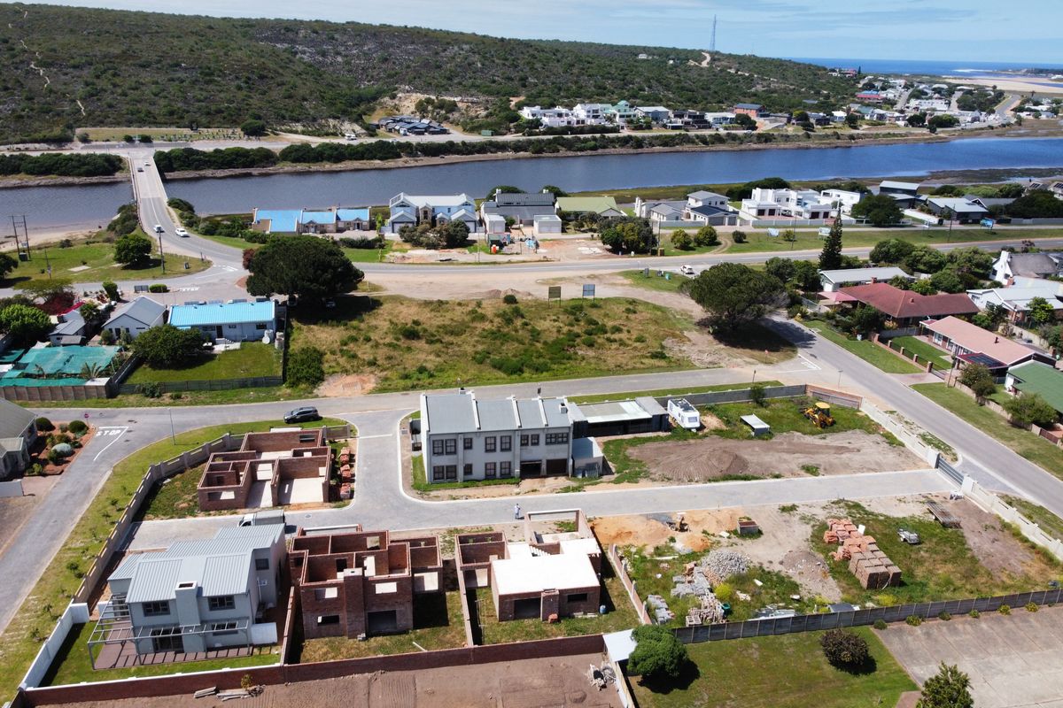 Aerial view of a residential development site featuring multiple plots with ongoing construction, paved access roads, and boundary walls in a coastal setting.