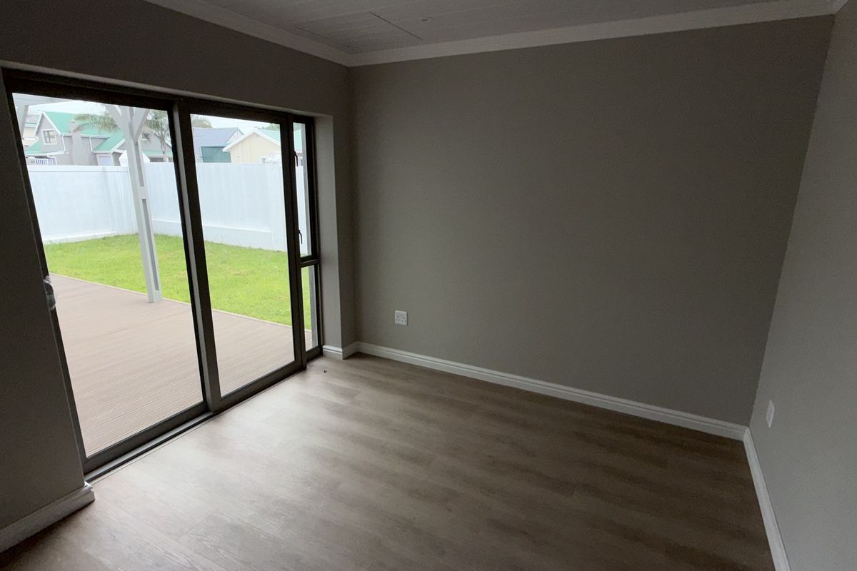 A bright, empty living room featuring modern laminate flooring, neutral walls, and large sliding glass doors that open onto an outdoor deck area.