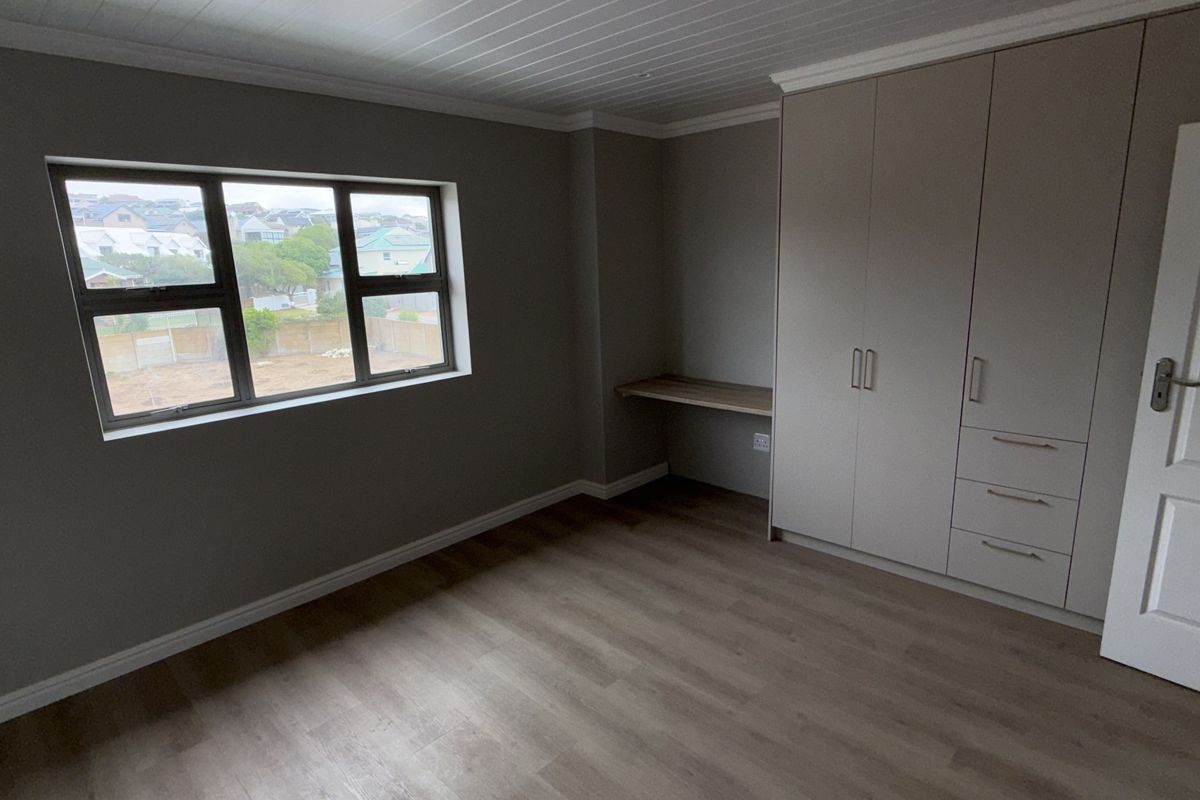 A bright, vacant bedroom featuring modern laminate flooring, a tongue and groove ceiling, built-in cupboards, and a convenient integrated desk area.