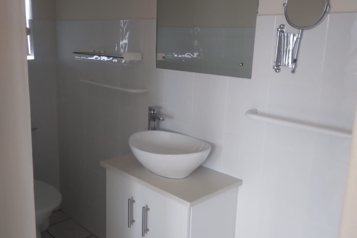 A clean, functional bathroom featuring a modern vessel sink on a white vanity cabinet, wall-mounted mirror, and neutral tiled finishes.