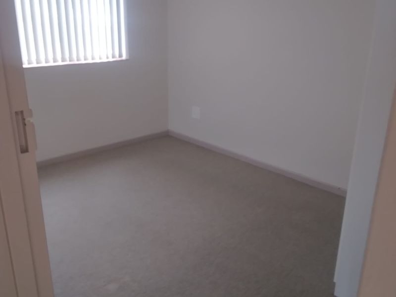 A clean, empty bedroom featuring neutral carpet flooring and vertical window blinds, providing a blank canvas for interior design.