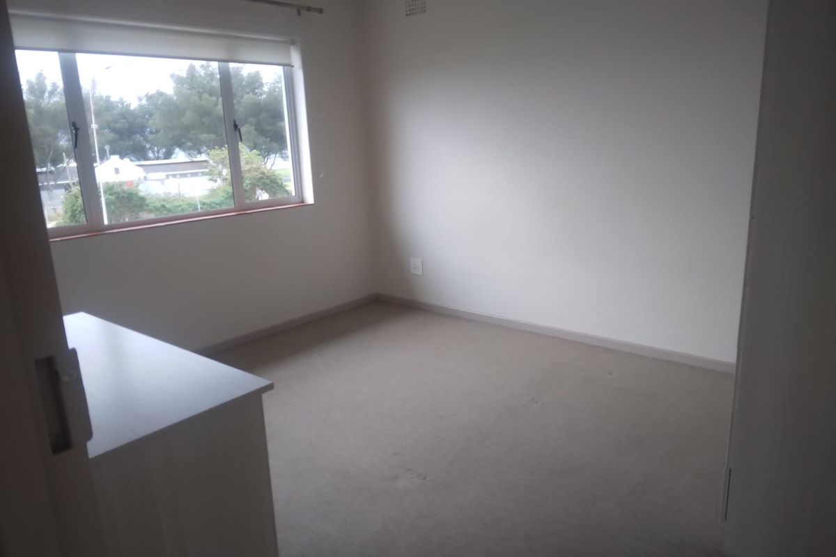 An empty bedroom featuring neutral carpeted flooring, a built-in cupboard, and a window with a roller blind.