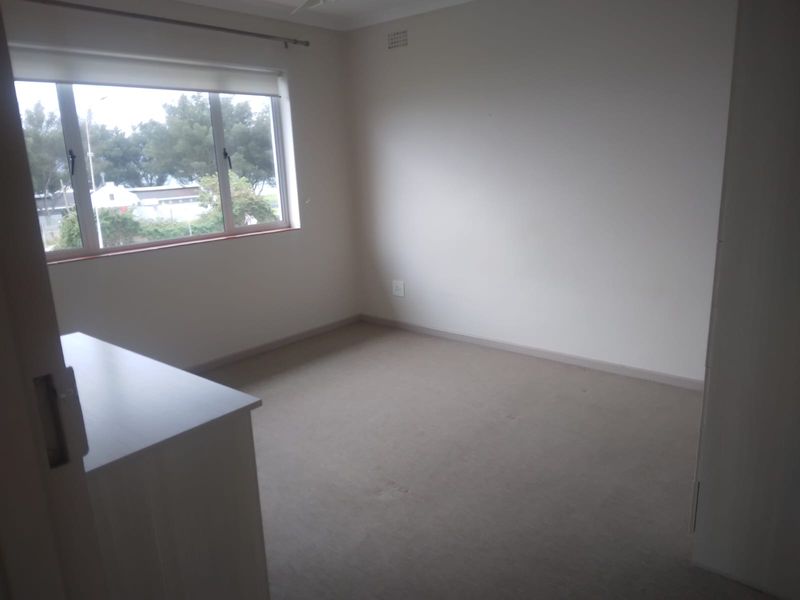 An empty bedroom featuring neutral carpeted flooring, a built-in cupboard, and a window with a roller blind.