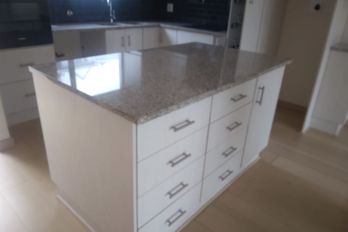 Modern kitchen featuring a central island with granite countertops, ample cabinetry, and integrated oven, set against a clean, neutral backdrop.