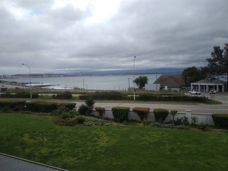A scenic elevated view overlooking a coastal landscape, featuring a well-maintained garden and boundary wall in the foreground with ocean views beyond.