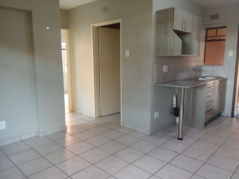 Open plan living area featuring tiled flooring and a compact kitchen with built-in cabinetry, granite countertops, and a stainless steel sink.