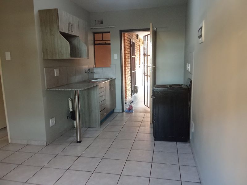 A functional kitchen area featuring built-in cabinetry, a stainless steel sink, and tiled flooring, with direct access to an exterior security gate.