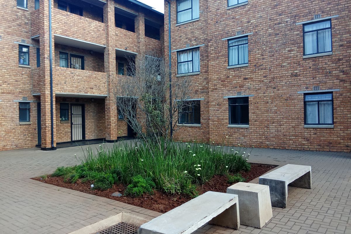 A well-maintained brick apartment courtyard featuring paved walkways, a central landscaped garden bed, and integrated concrete seating areas.