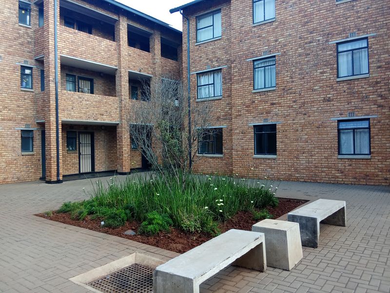 A well-maintained brick apartment courtyard featuring paved walkways, a central landscaped garden bed, and integrated concrete seating areas.