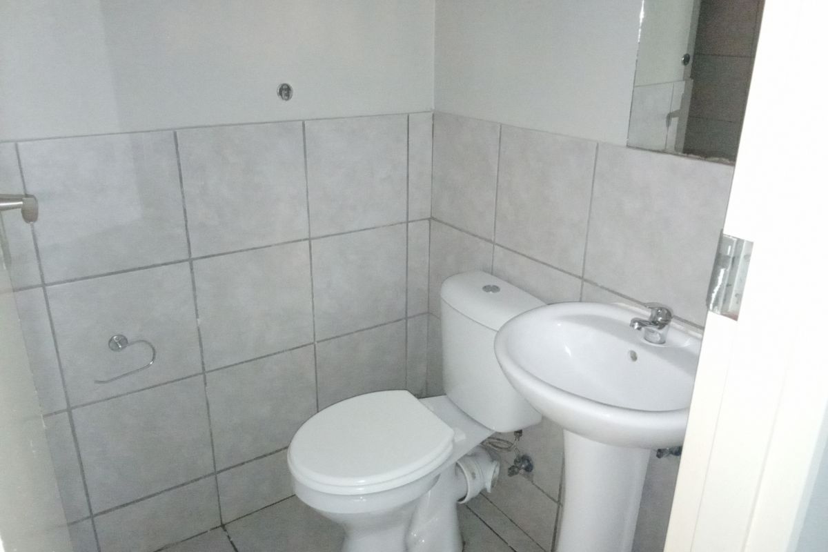 A functional bathroom featuring a pedestal basin, toilet, and neutral wall and floor tiling.