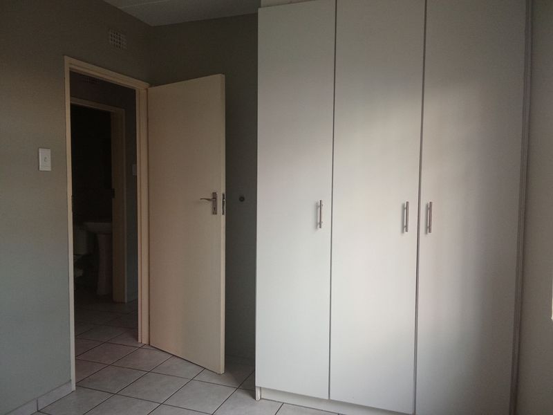 A bedroom featuring built-in cupboards and tiled flooring, with an adjacent doorway leading to a bathroom area.