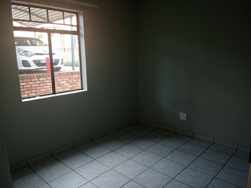 An empty bedroom featuring neutral tiled flooring and a window providing natural light.