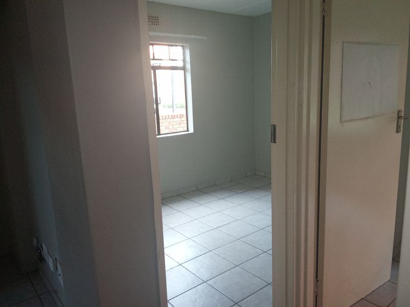 An empty bedroom featuring tiled flooring and a window, viewed from the adjacent hallway.