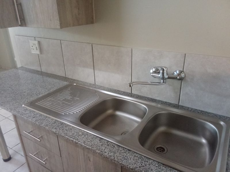 A clean and functional kitchen area featuring a double bowl stainless steel sink, chrome mixer tap, and modern laminate cabinetry with granite-look countertops.