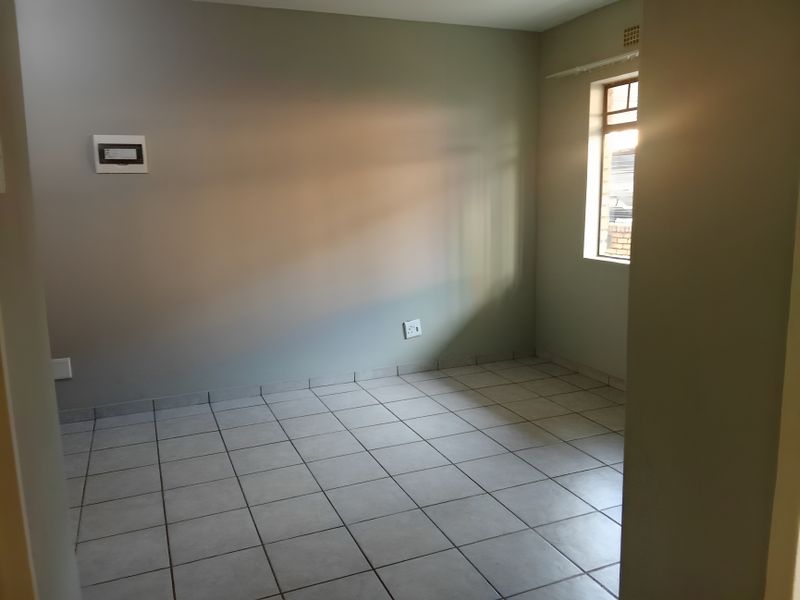 An empty bedroom featuring neutral wall paint, tiled flooring, and a window providing natural light.