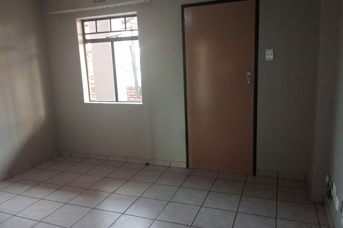 An empty bedroom featuring neutral tiled flooring, a window with security bars, and a standard internal door.