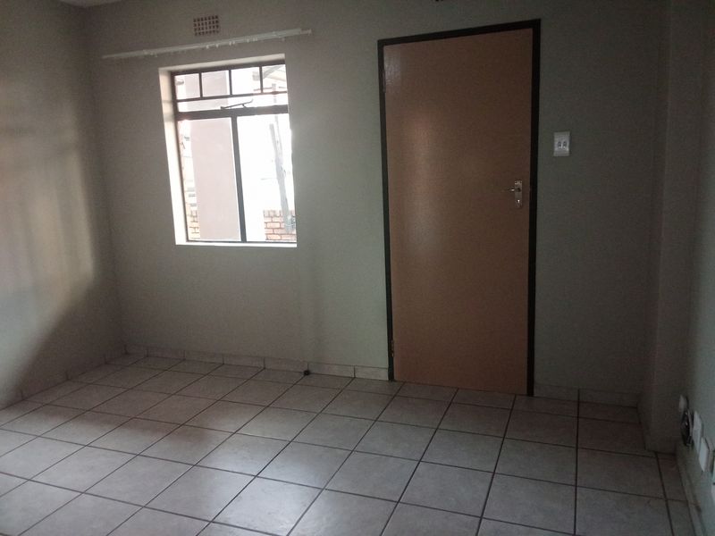 An empty bedroom featuring neutral tiled flooring, a window with security bars, and a standard internal door.