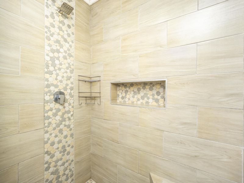 A modern shower enclosure featuring wood-look ceramic wall tiles, a decorative mosaic accent strip, and a built-in recessed storage niche.