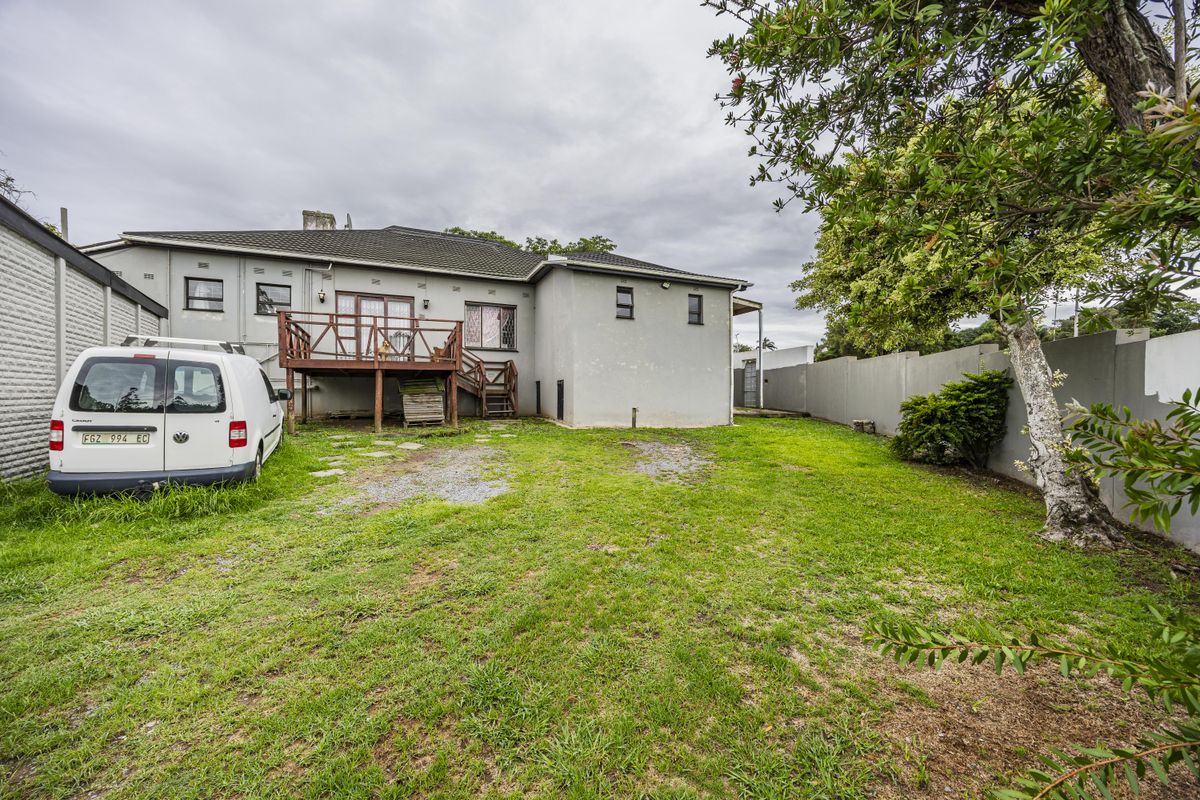 Rear view of the property featuring a raised timber deck, a large grassed backyard, and perimeter boundary walls.