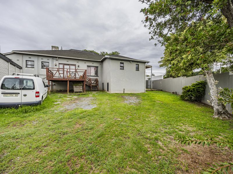 Rear view of the property featuring a raised timber deck, a large grassed backyard, and perimeter boundary walls.