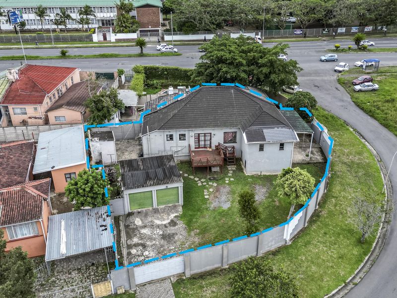 Aerial view of a residential property featuring a tiled roof house, double garage, wooden deck, and enclosed garden area with perimeter walling.