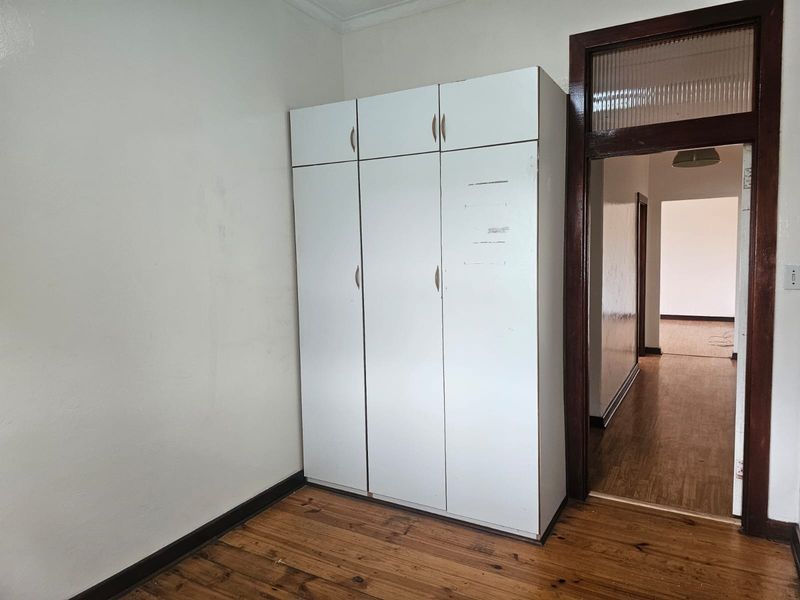 A bedroom featuring original timber flooring, a built-in wardrobe, and a classic timber door frame with a ribbed glass transom window.