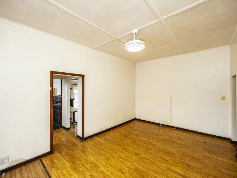 An empty living room featuring parquet flooring, a ceiling fan, and a timber door frame leading to an adjacent space.